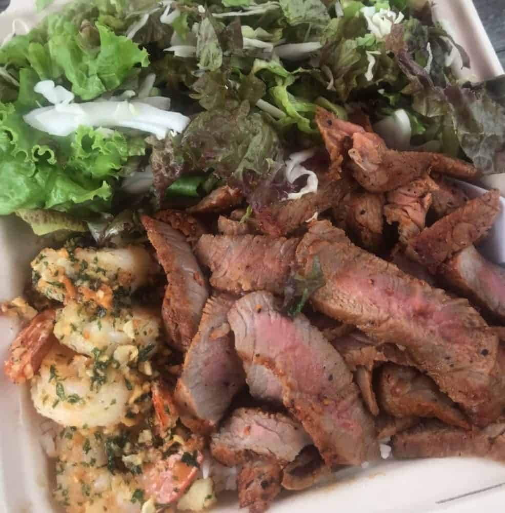 Island steak and garlic butter shrimp surf and turf plate with fresh greens over rice